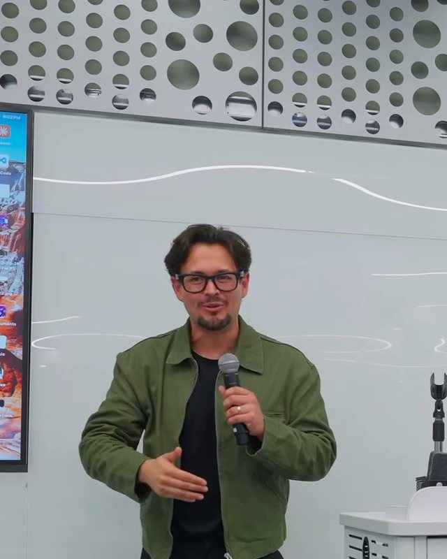José Vásquez dando clase de pie frente a pantallas en una sala